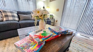 Een woonkamer met een bank, een bijzettafeltje met gezelschapsspellen, een vaas met bloemen en een decoratief bord aan de muur.