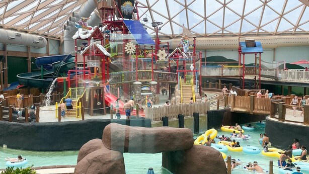 Een overdekt waterpark met een groot zwembad, glijbanen en diverse speelconstructies.