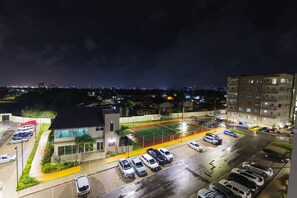 A parking lot with multiple cars, a tennis court, and a building with a modern design.