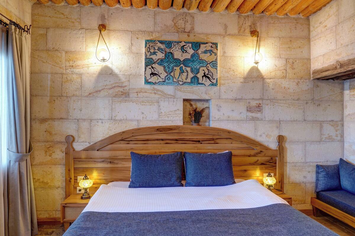 Een kamer met een houten bed, twee bedlampen, een wandlamp en een decoratieve tegel.