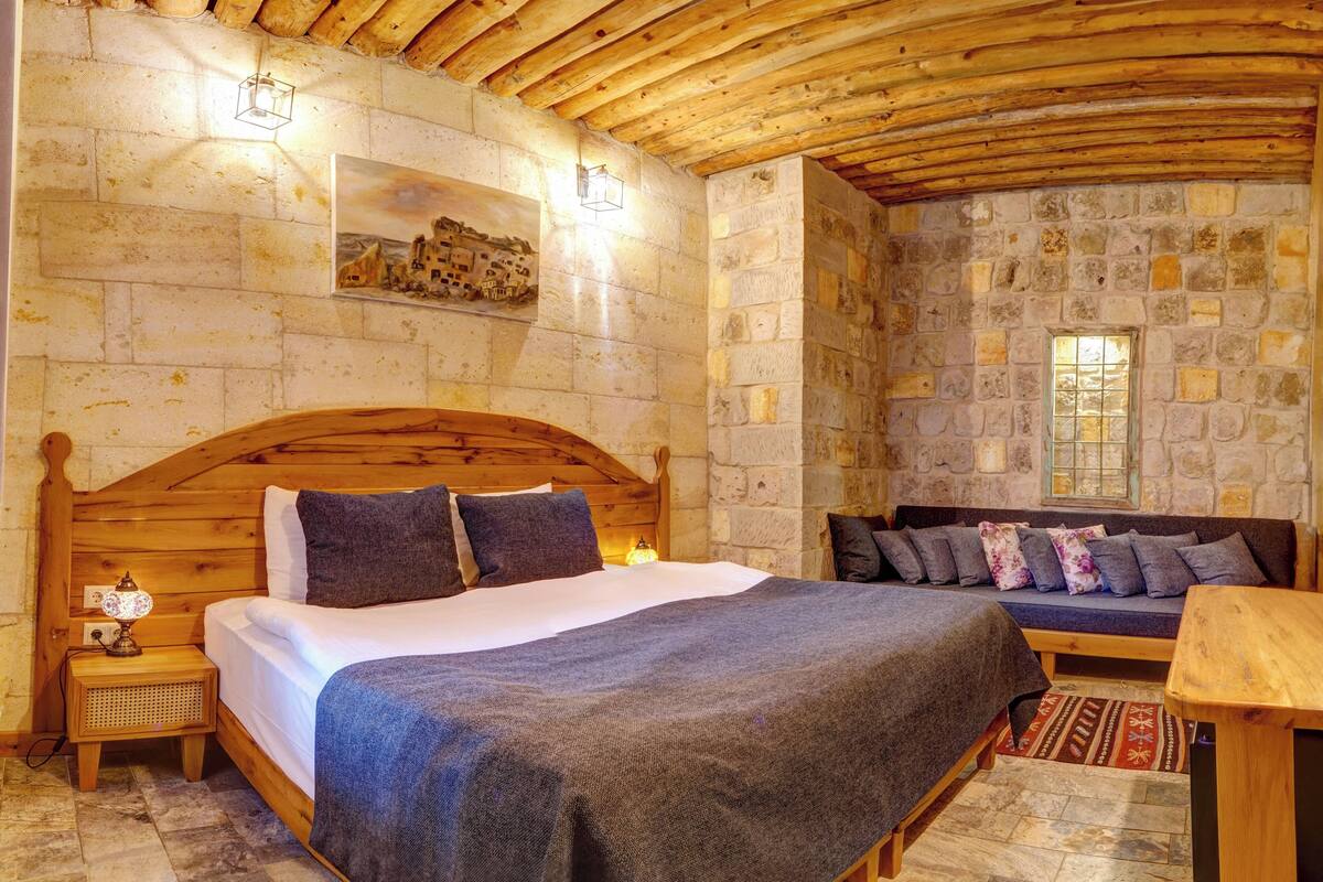 Een knus vertrek met een houten bed, een bank, stenen muren en een stenen vloer.