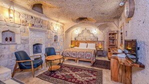 A rustic room with a stone fireplace, a bed with patterned bedding, a wooden desk, and a television.