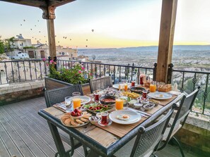 A table set for breakfast on a balcony with a scenic view, including hot air balloons in the distance. - Vasıl Cave Hotel (Nevsehir)