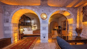 A room with a bed, a sofa, a chair, a small table, and a decorative rug. There are two arches in the room.