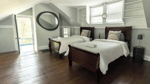 A bedroom with two beds, a large mirror, and a window with blinds.