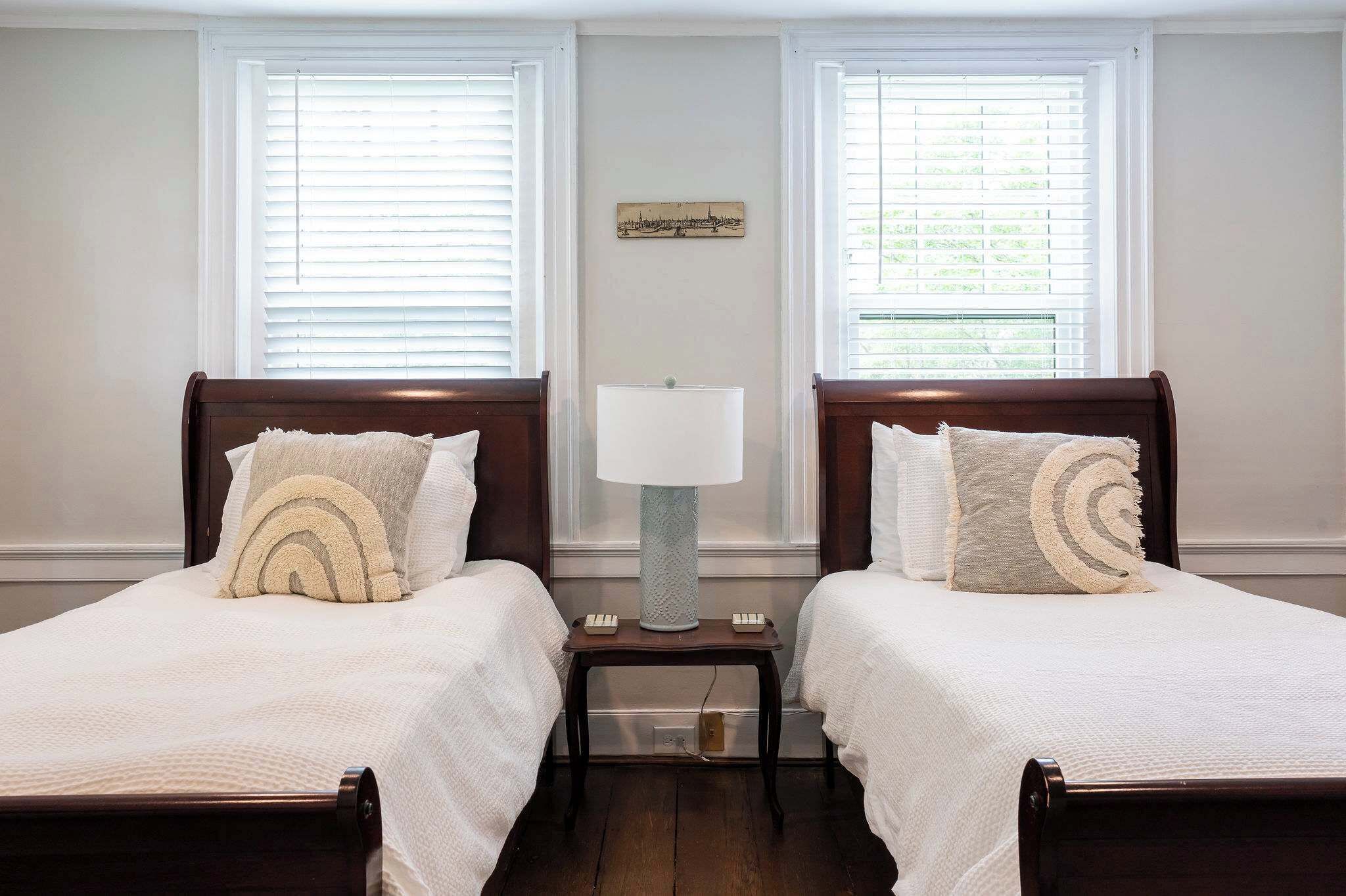A double bed with a white bedspread and two pillows, a nightstand with a lamp, and a wall-mounted artwork.