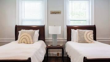 A double bed with a white bedspread and two pillows, a nightstand with a lamp, and a wall-mounted artwork.