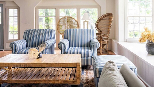 A room with a large window, two striped armchairs, a rattan chair, a wooden coffee table, and a patterned rug.