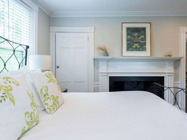 A bedroom with a bed, a fireplace, a door, and a framed picture on the wall.
