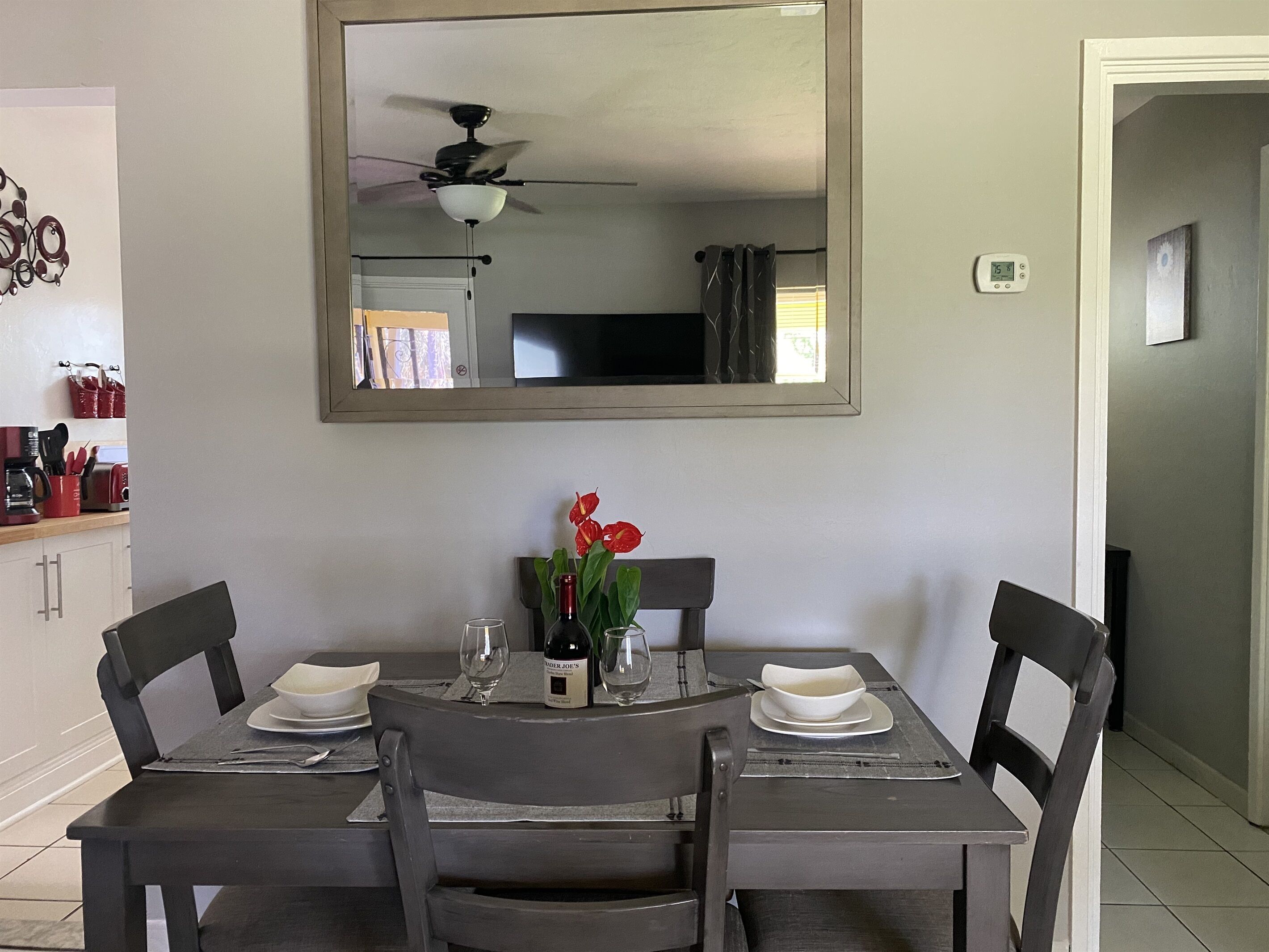 A dining area with a table set for two, a mirror above the table, and a ceiling fan.