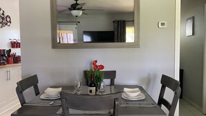 Zona pranzo con tavolo apparecchiato per due, uno specchio sopra il tavolo e una ventola a soffitto.