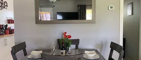 A dining area with a table set for two, a mirror above the table, and a ceiling fan.