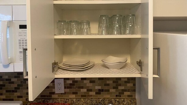 Una cucina con un armadietto bianco contenente bicchieri da vino, calici e piatti.
