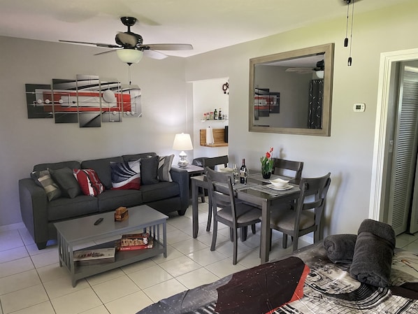 A living room with a sofa, coffee table, dining table, chairs, and a ceiling fan.