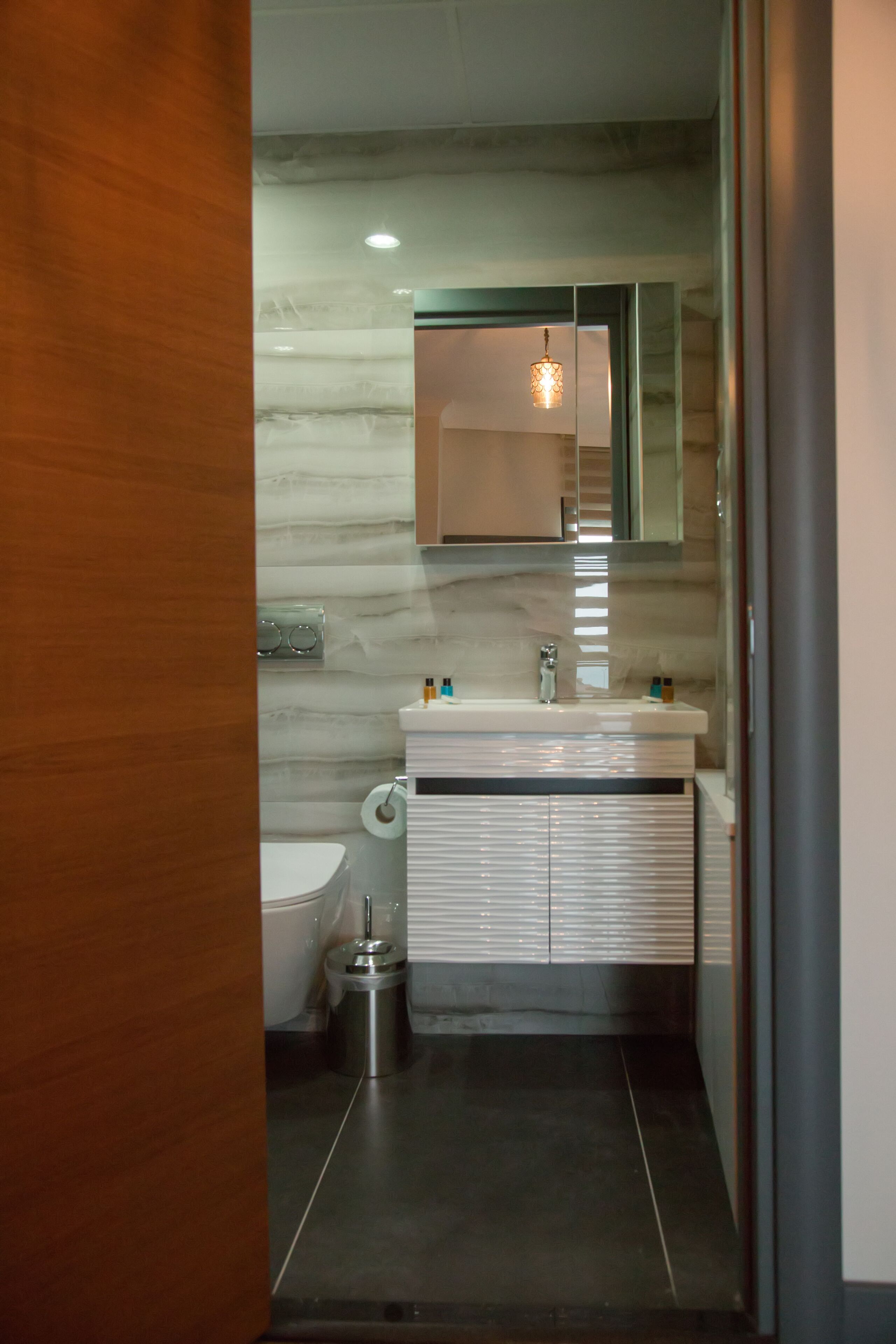 A modern bathroom with a marble wall, a white sink, and a mirror above it.