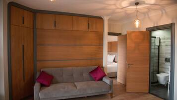 Una habitación moderna con un sofá gris, un armario de madera y una puerta de cristal que da al baño.