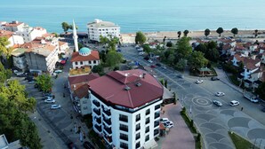 Un paysage urbain côtier avec une mosquée imposante, un bâtiment circulaire surmonté d’un dôme, et des immeubles résidentiels aux toits recouverts de tuiles rouges.