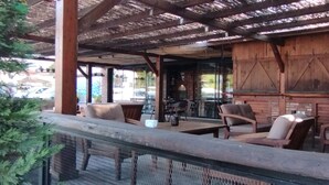 Un espace extérieur aménagé avec des tables et des chaises en bois, un toit de chaume et une vue sur la rue.