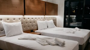 Une chambre d’hôtel avec deux lits, une tête de lit en bois et une vue sur la ville de nuit.