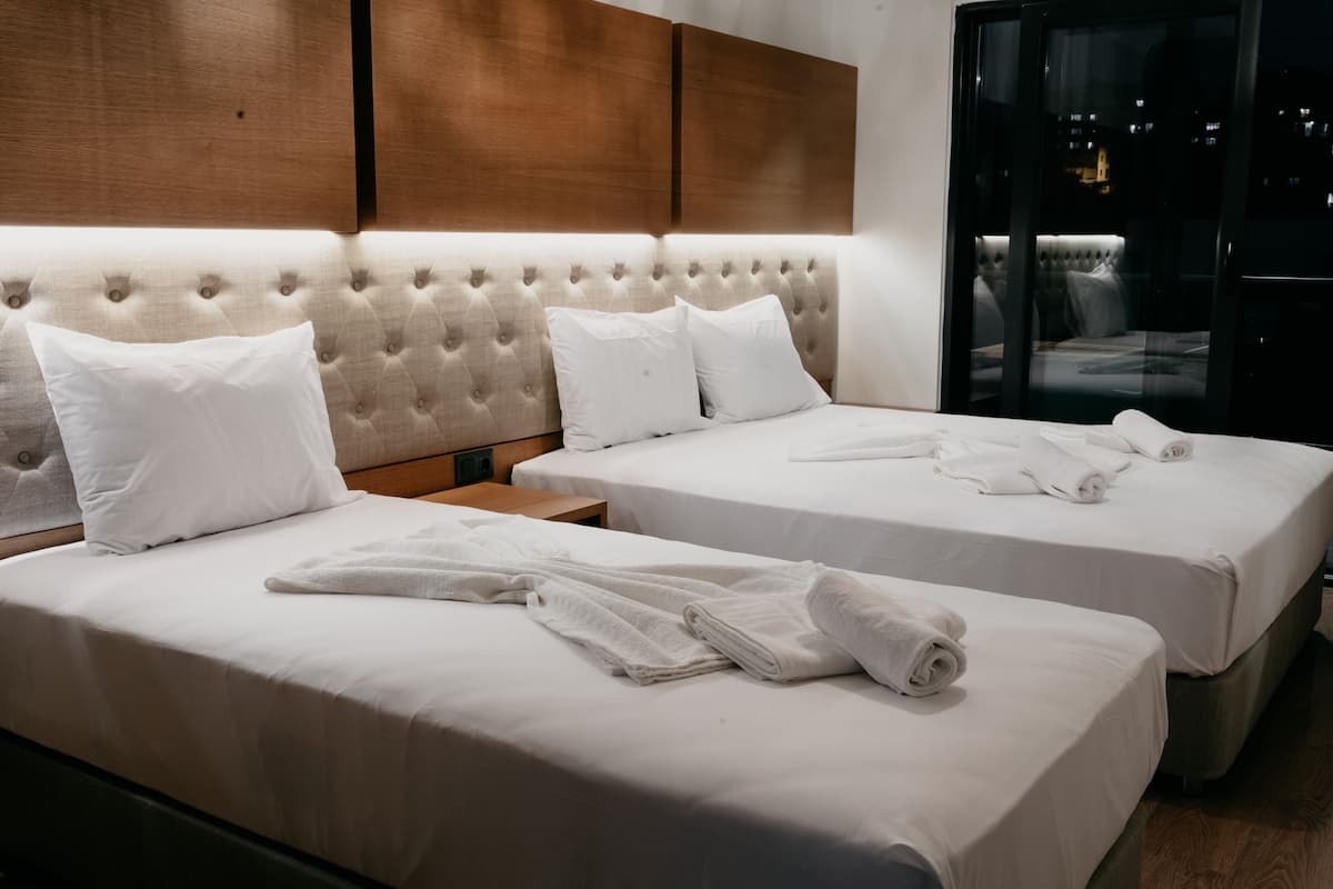 A hotel room with two beds, a wooden headboard, and a view of the city at night.