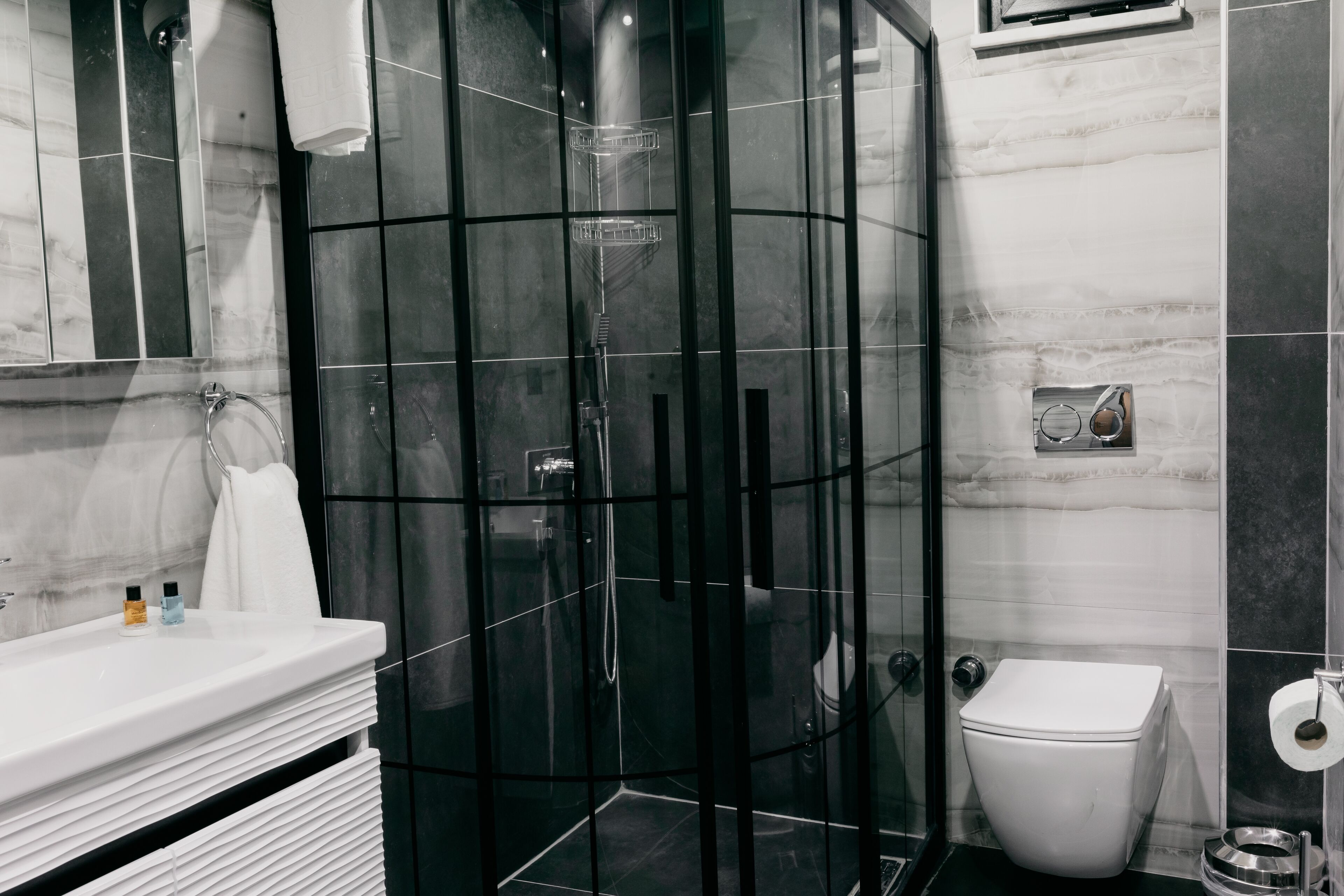 A modern bathroom with a glass-enclosed shower, a white toilet, and a marble-tiled wall.