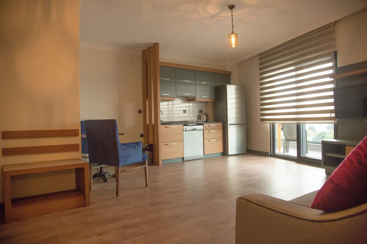 A modern kitchen with wooden cabinets, a built-in oven, and a dishwasher. There is a dining area with a bench and a chair.