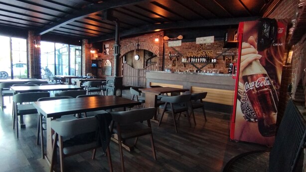 Un restaurant avec des tables et des chaises en bois, des murs en briques et un bar où sont exposées des bouteilles.