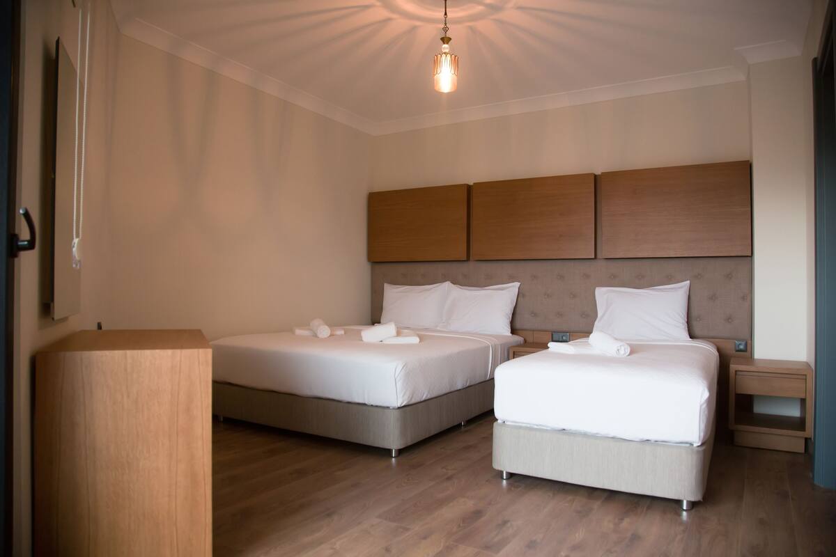 A hotel room with two beds, a wooden headboard, a bedside table, and a hanging light fixture.