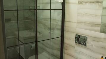 Un baño moderno con ducha de vidrio, inodoro blanco y pared con azulejos de mármol.