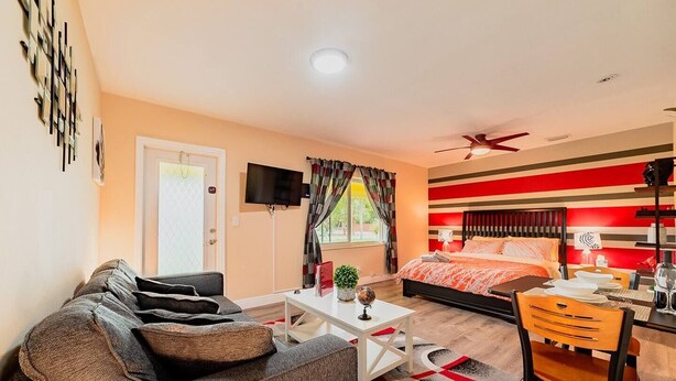 A modern hotel room with a sofa, a dining table, a bed with a red and white striped headboard, a ceiling fan, and a TV on the wall. - ✨ #3 Studio close to Bike Rental and Beach (Fort Lauderdale)