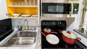A kitchen with a sink, stove, and microwave. There are pots and pans on the stove, and a bottle of water on the counter. - ✨ #3 Studio close to Bike Rental and Beach (Fort Lauderdale)