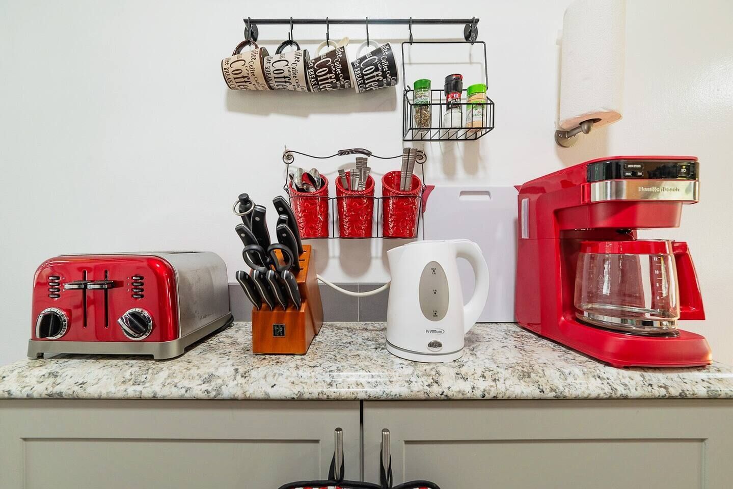 A kitchen with a red toaster, a white kettle, a red coffee maker, and a knife block.