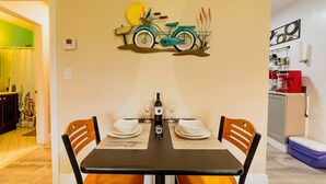 A dining area with a table set for two, a wall-mounted bicycle decoration, and a kitchen area in the background. - ✨ #3 Studio close to Bike Rental and Beach (Fort Lauderdale)