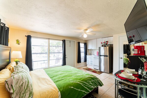 A compact hotel room with a bed, a small kitchenette, and a dining area.