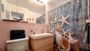 Een badkamer met een houten wastafelmeubel, toilet en douchegordijn versierd met zeesterren en schelpen.