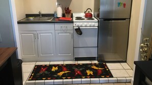 Eine Küche mit weißen Schränken, einem Herd, einem Kühlschrank und einem farbenfrohen Teppich.