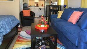 Ein Wohnzimmer mit zwei Sofas, einem Couchtisch mit Blumenvase und einer Küche im Hintergrund.
