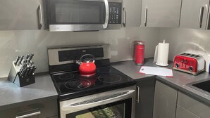 Moderni keittiö, jossa on ruostumattomasta teräksestä valmistettu mikroaaltouuni, liesi ja uuni. Liedellä on punainen vedenkeitin, leivänpaahdin ja työtasolla punainen muki.