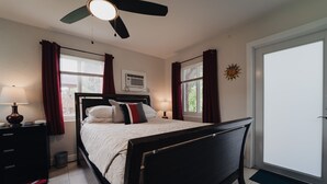 Quarto com cama, duas mesas de cabeceira, um ventilador de teto e janela com cortinas.
