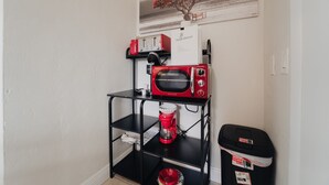Uma área de cozinha com uma prateleira preta contendo um micro-ondas vermelho, uma cafeteira e uma lixeira.