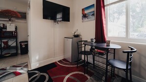 Um espaço compacto com cozinha compacta, televisão de tela plana, mini-geladeira, mesa de jantar com cadeiras, mesa de centro e janela com cortinas.