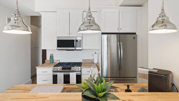 A modern kitchen with white cabinets, stainless steel appliances, and pendant lighting. - Clover Haven | High Rise | Down Town South Bend ND (South Bend)