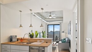 A modern kitchen with a wooden countertop, stainless steel appliances, pendant lighting, and a view to the living area. - Clover Haven | High Rise | Down Town South Bend ND (South Bend)