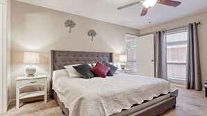 Een slaapkamer met een groot bed, een plafondventilator en een raam met gordijnen.
