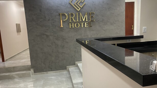 A hotel reception area with a marble floor, a reception desk, and a wall with the hotel's name in gold lettering. - Hotel prime (São Paulo)