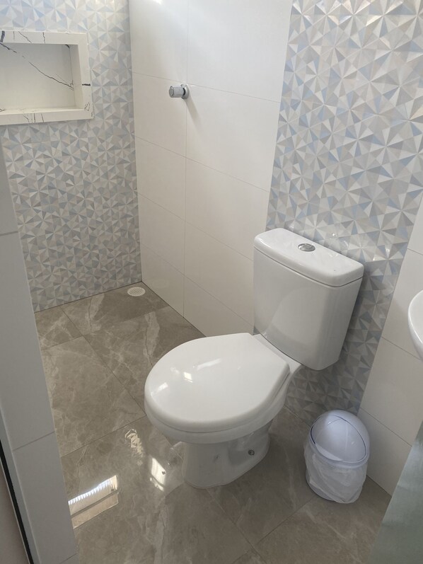 Un baño con inodoro, lavamanos y un cubo de basura.