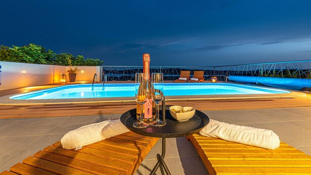 A rooftop pool area with a table set for two, a bottle of champagne, and a bowl of olives. - Gorgeous home in Sibenik (Sibenik)