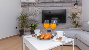 A modern living room with a white table set for breakfast, a flat-screen TV mounted on a textured wall, and a grey sofa. - Gorgeous home in Sibenik (Sibenik)