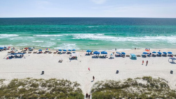 Een strand met rijen parasols en ligbedden, een helder uitzicht op de oceaan en een zandvlakte met schaarse begroeiing.