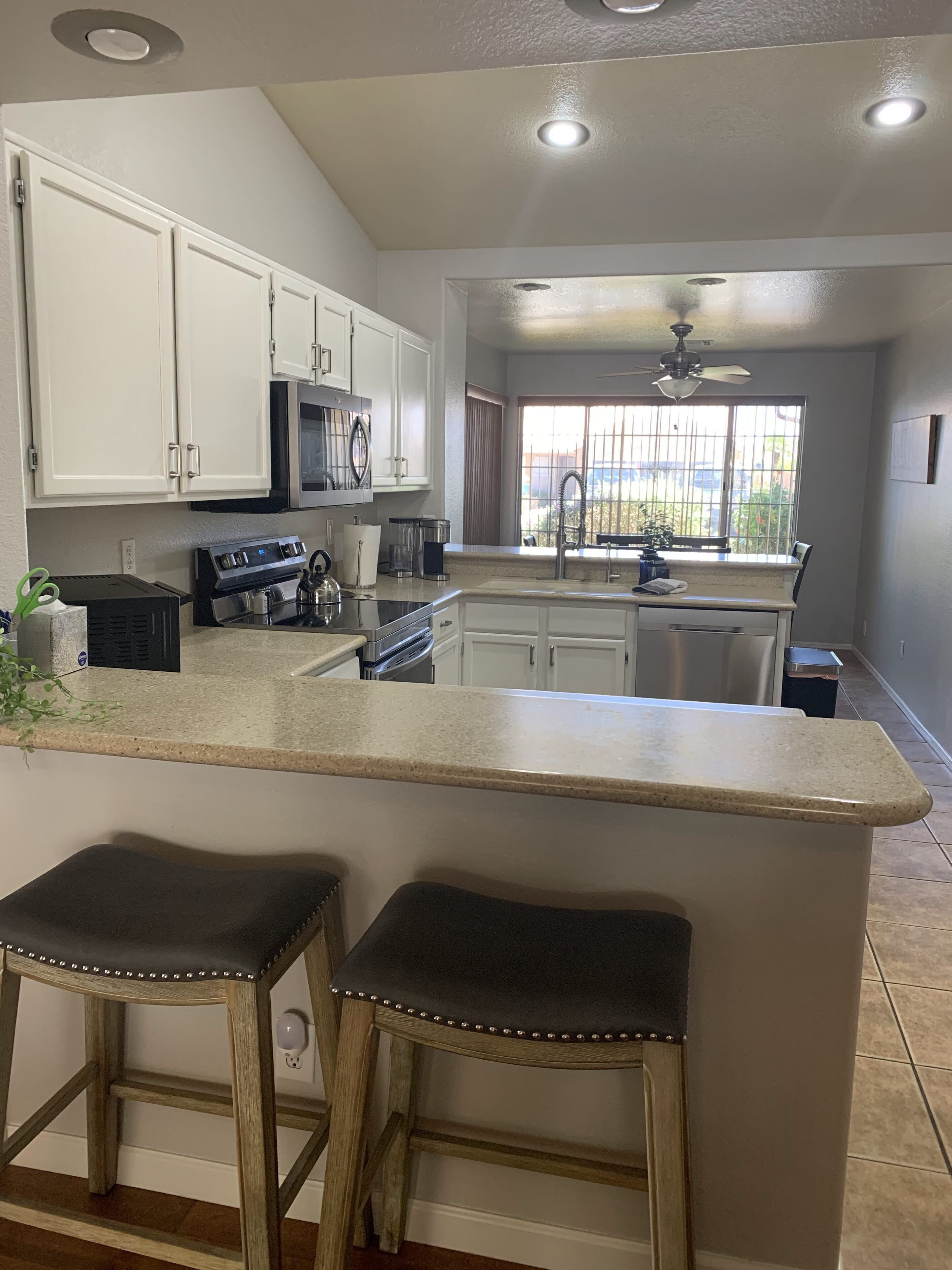 A modern kitchen with white cabinets, a central island with stools, a microwave, and a stove.